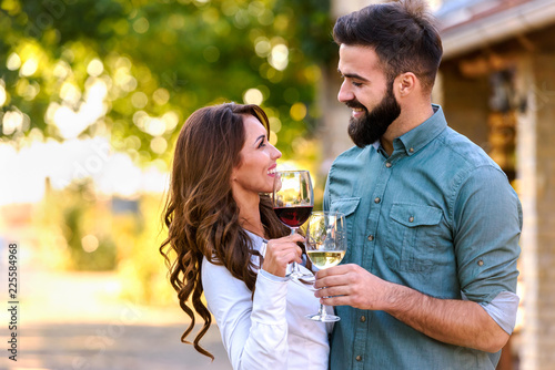 Portrait of young smiling man and woman tasting wine at winery vineyard - Young people enjoying harvest time together. Romantic love.
