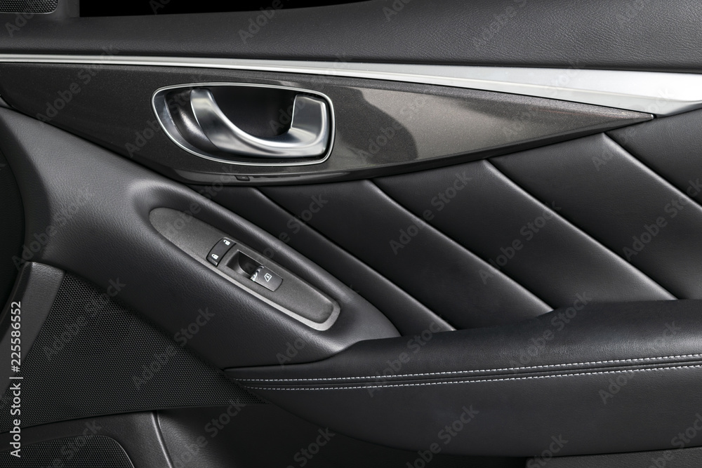 Door handle with Power window control buttons of a luxury passenger car. Black perforated leather interior with stitching of the luxury modern car. Modern car interior details. Car detailing.