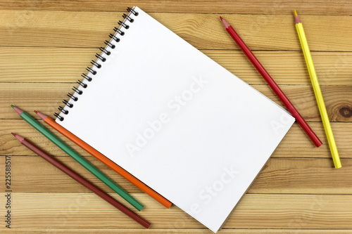 on a wooden table is a notepad with colored pencils