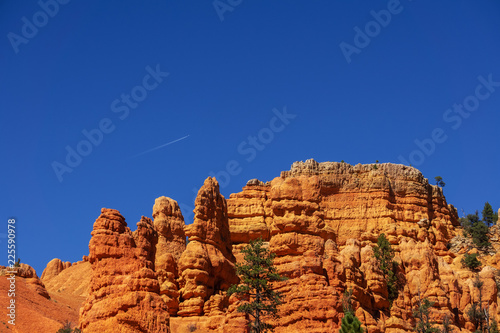 white trail of an airplane in the blue sky over the orange mountains of utah