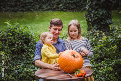Happy halloween. Father and two daughters look at the face cut in the pumpkin for Halloween outside.