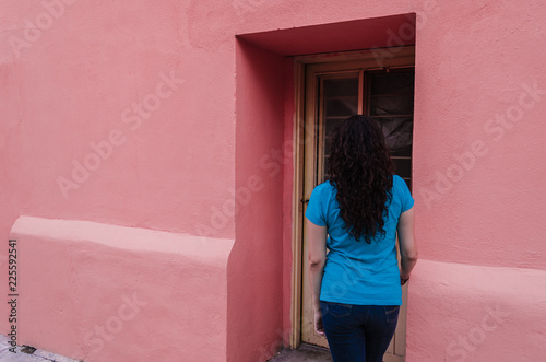 Girl in a blue shirt breaks at the door of a pink house. © Dany Rocha
