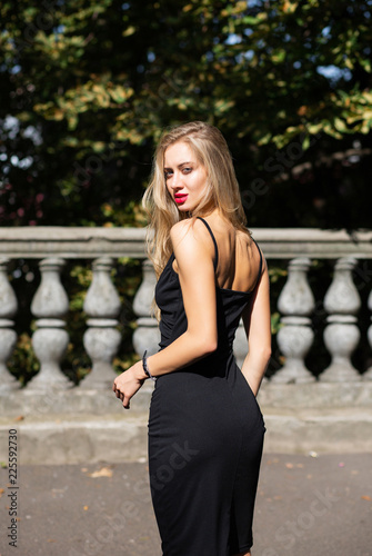 Outdoor shot of seductive blonde woman with lush hair wearing black skinny dress