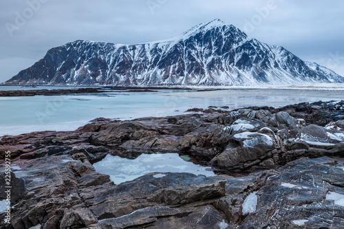 Rocky coast of fjord of Norwegian sea in winter, snowy mountains in background. Lofoten islands, Norway