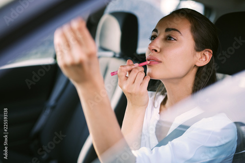 woman driver looking at rear view mirror and correcting the makeup while driving the car