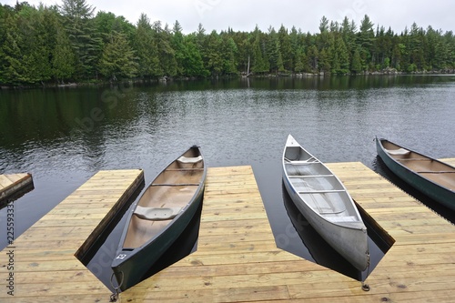 Sagamore Lake, Adirondack Park, New York, USA: Canoes tied to a wooden dock on a lake surrounded by evergreen trees.