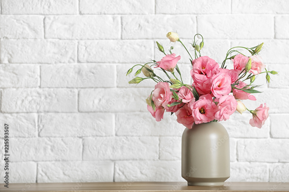 Obraz premium Vase with beautiful flowers on table against brick wall, space for text