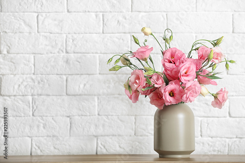 Fotografija Vase with beautiful flowers on table against brick wall, space for text