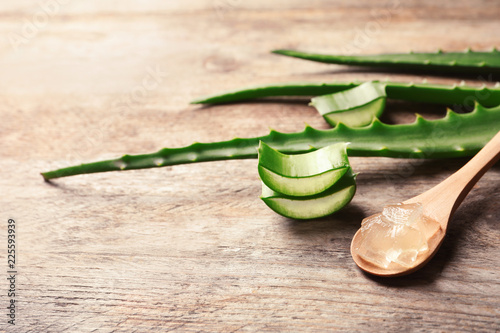 Spoon with aloe vera gel on wooden background. Space for text