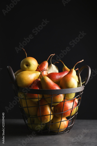 Basket with ripe pears on table against black background. Space for text
