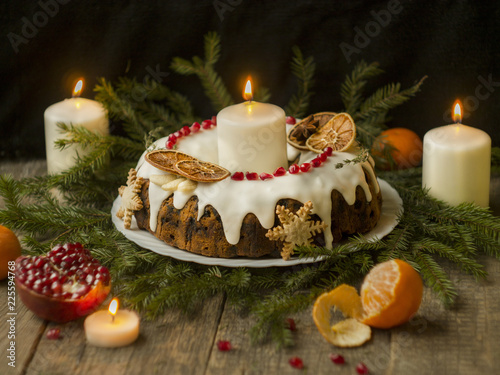 Christmas English fruitcake with candied fruit  dried fruit and nuts  decorated with white icing on a wooden background with fir branches  candles. Festive English cuisine
