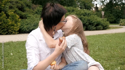 Happy Mother and Daughter gently hug and kiss sitting on a Blanket at Park Picnic photo