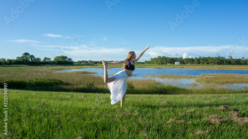 blonde woman spiritual doing yoga king dance standing pulling bow Natarajasana / Dandayamana Dhanurasana pose in nature