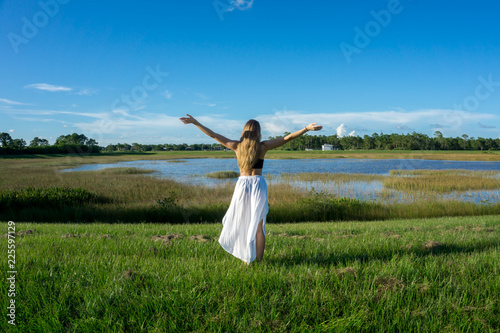 Blonde young woman standing backwards in a beautiful field landscape outdoors with raise hands arms to the sky