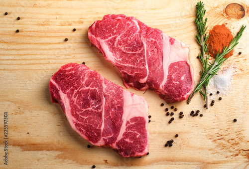 two raw beef neck steak on wooden background with seasonings prepared for cooking