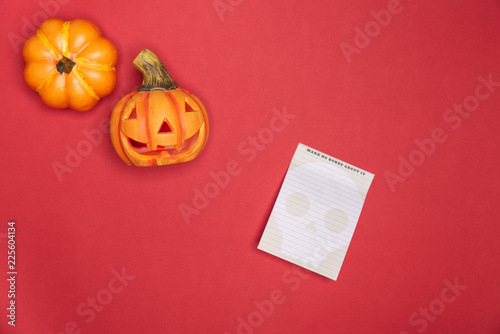 Halloween sculpted pumpkin funny and cute face along with full intact pumkin along notes paper on red background