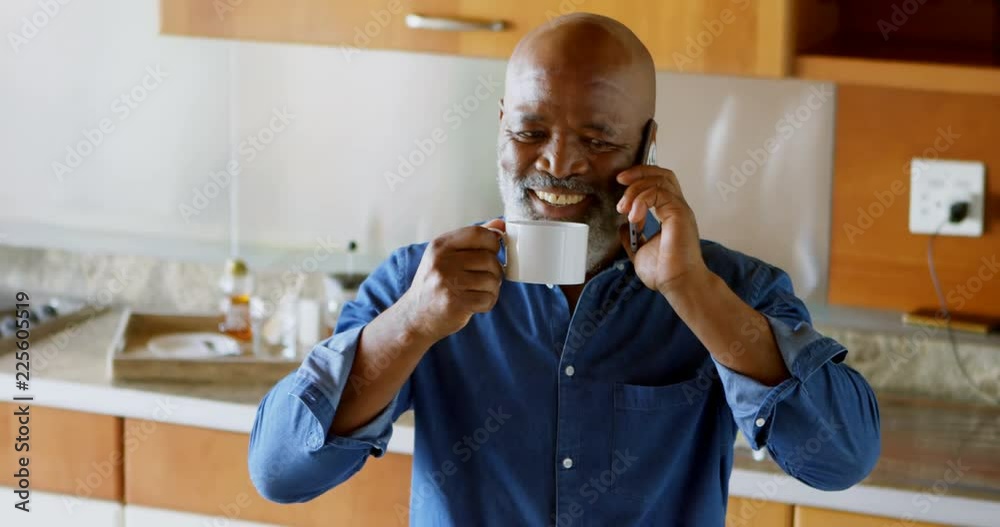Senior man having black coffee while talking on mobile phone in kitchen 4k