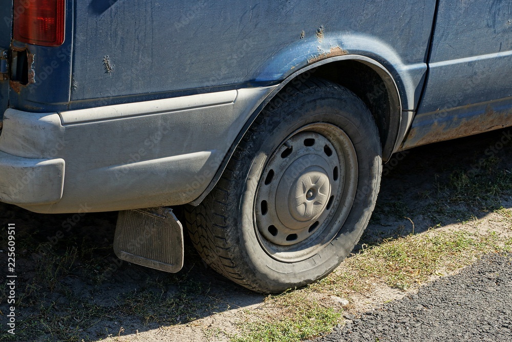 part of a gray dirty car with a rear wheel and bumper on asphalt