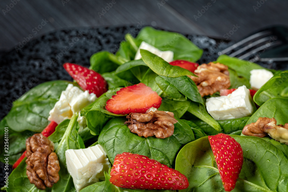 Strawberry spinach salad with feta cheese, walnuts, olive oil, on black plate, on dark background Strawberry spinach salad with feta cheese, walnuts, olive oil, on black plate, on dark background
