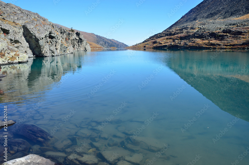 Россия, Республика Алтай, прозрачная вода и скалистые берега озера Акчан в безветренную погоду