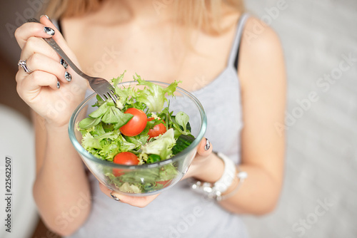 Close-up rear view woman holding bowl of fresh vegetable salad holding fork in hand.