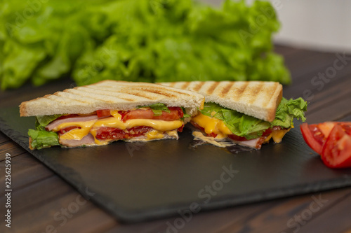 Sandwich with ham, tomatoes, cheese and lettuce on dark background