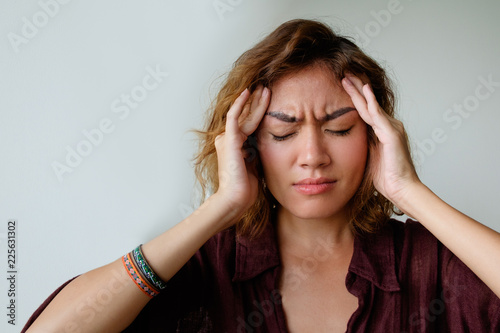 Upset girl suffering from headache. Closeup of young Asian woman with pain grimace holding head and touching temples. Head ache concept