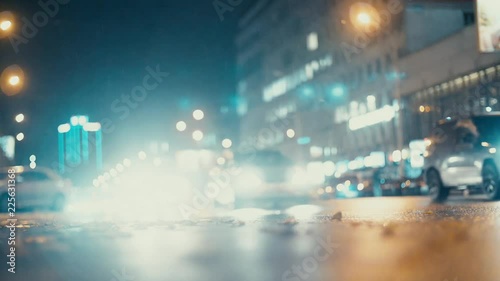 City lights and cars driving in traffic background. Autumn leaves scatter along the night road from the wind from passing cars. Out of focus background with blurry city lights and car light.