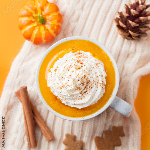 Pumpkin latte with spices. Boozy cocktail with whipped cream on top on knitted scarf. Orange background.