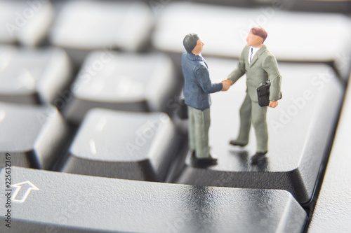 Business deal or agreement and success concept. Two miniature businessmen shaking hands while standing on the keys of a black keyboard.