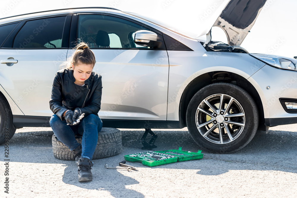 Upset woman with different wrenches and broken car