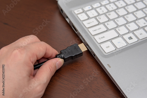 Man is connecting black hdmi cable into laptop. photo