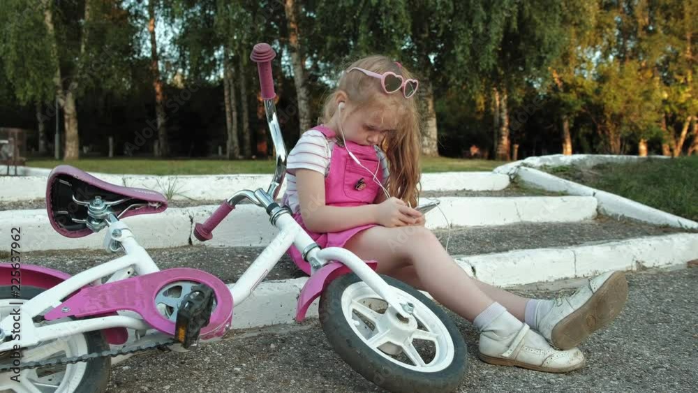 A little beautiful girl in a pink dress is sitting in the park on the ...