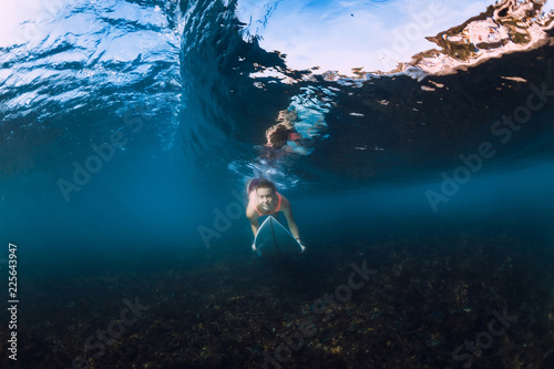 Underwater view of surfer girl with surfboard dive under barrel wave