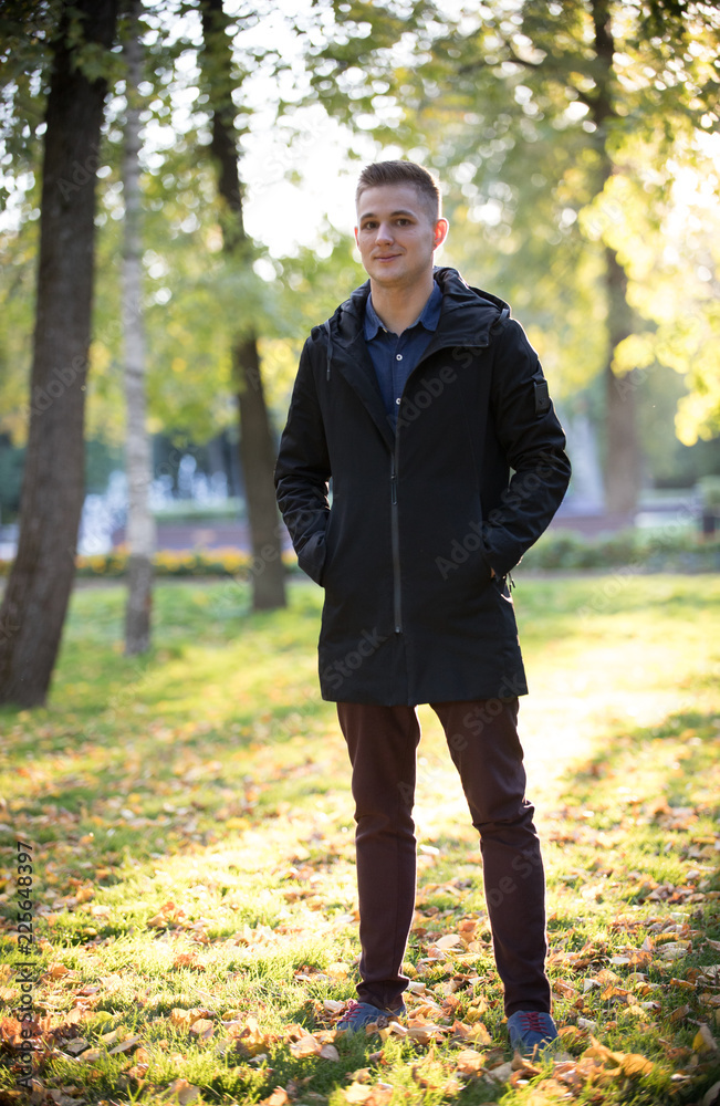 Handsome and young man in a black jacket standing in the park