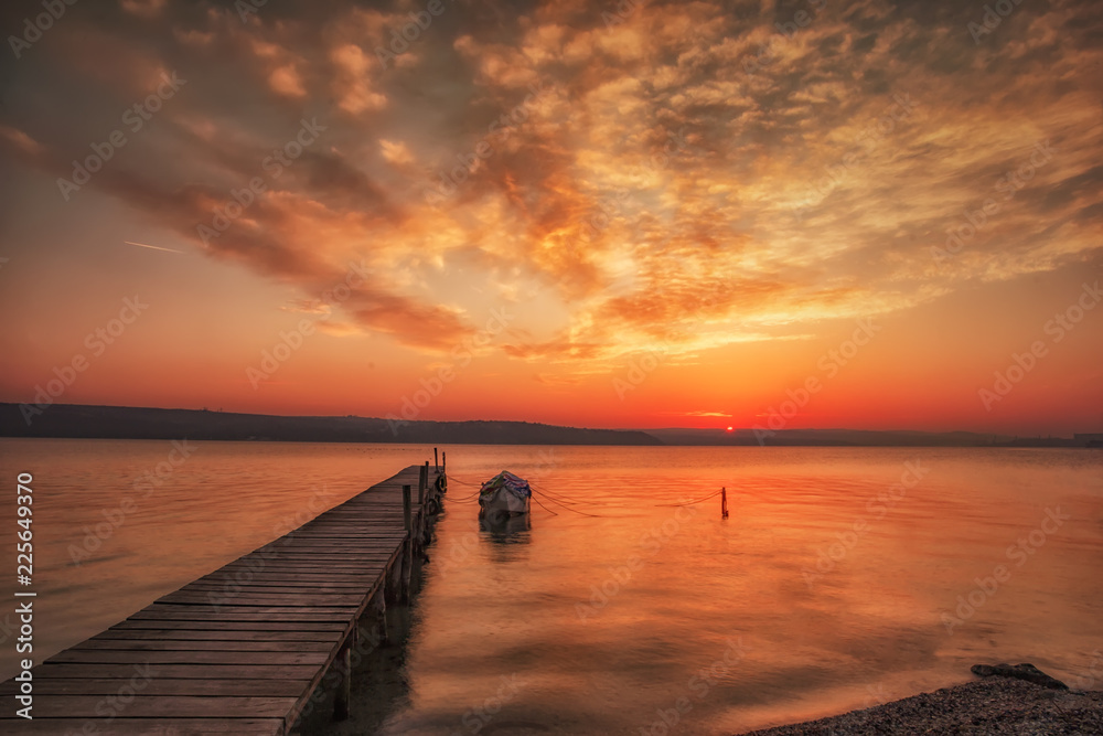 Amazing sunset/sunrise at a shore with wooden pier and fishing boat