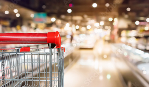 Empty red shopping cart with abstract blur supermarket discount store aisle and product shelves interior defocused background
