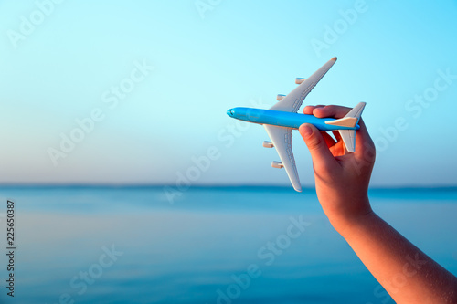 A hand holding a toy aircraft above the water at sunset