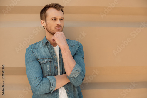 thoughtful young man looking away in front of wall