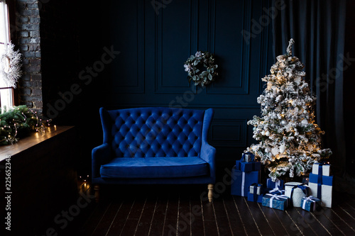 Decorated dark blue living room with beautiful Christmas tree and cozy velvet sofa