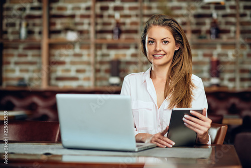 Businesswoman using tablet while sitting in cafeteria. On table laptop and coffee.