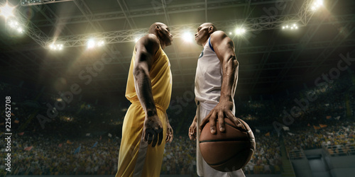 Two black basketball players on big professional arena before the game. Two teams. Players collided face to face. Player holds a ball © Alex