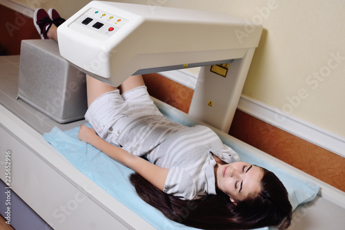 young pretty girl on examination in a modern clinic by densitometry - checking the density of bone tissue. photo