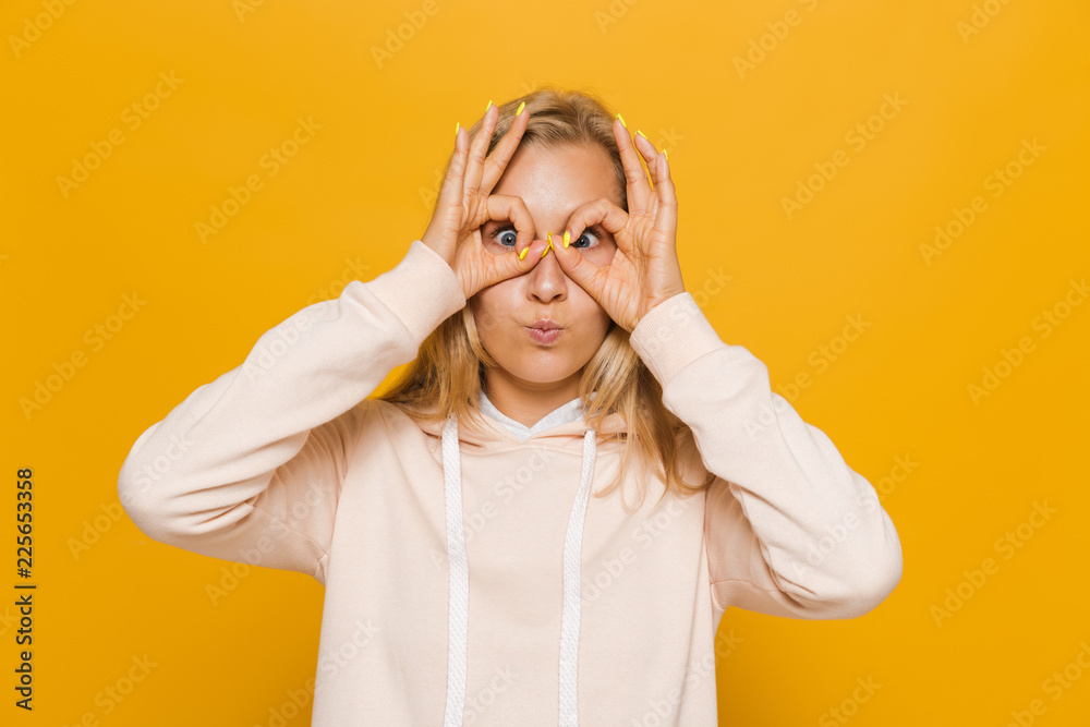 Photo of amusing girl 16-18 with dental braces looking at camera through holes made with fingers, isolated over yellow background Photo of amusing girl 16-18 with dental braces looking at camera through holes made with fingers, isolated over yellow background