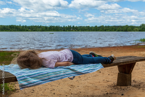 Flicka ligger på en träbänk vid en sjö photo