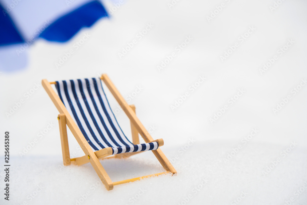 A blue, wooden, striped wooden beach chair in the snow.