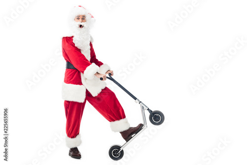 surpised santa claus in costume riding on kick scooter isolated on white background