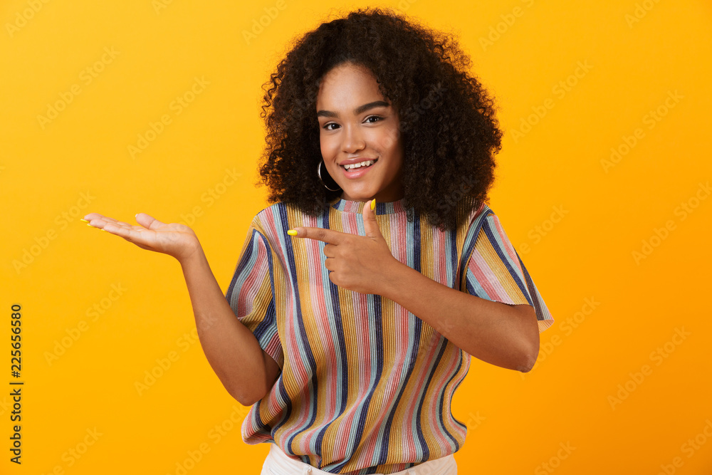 Happy young african cute girl posing isolated over yellow background pointing to copyspace. Happy young african cute girl posing isolated over yellow background pointing to copyspace.