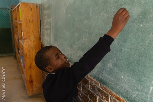 Schoolboy writing on chalkboard in classroom photo