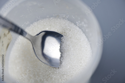 A spoonful of granulated sugar on gray background